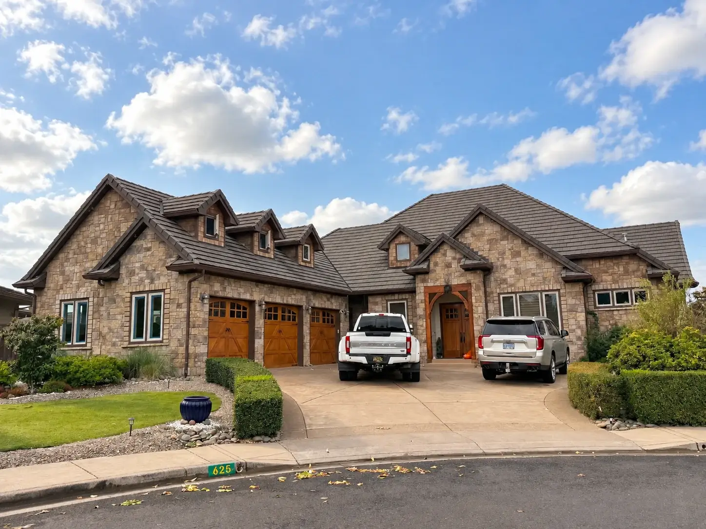 Stone-front home with a tile roof, dormer windows, and three wood carriage garage doors