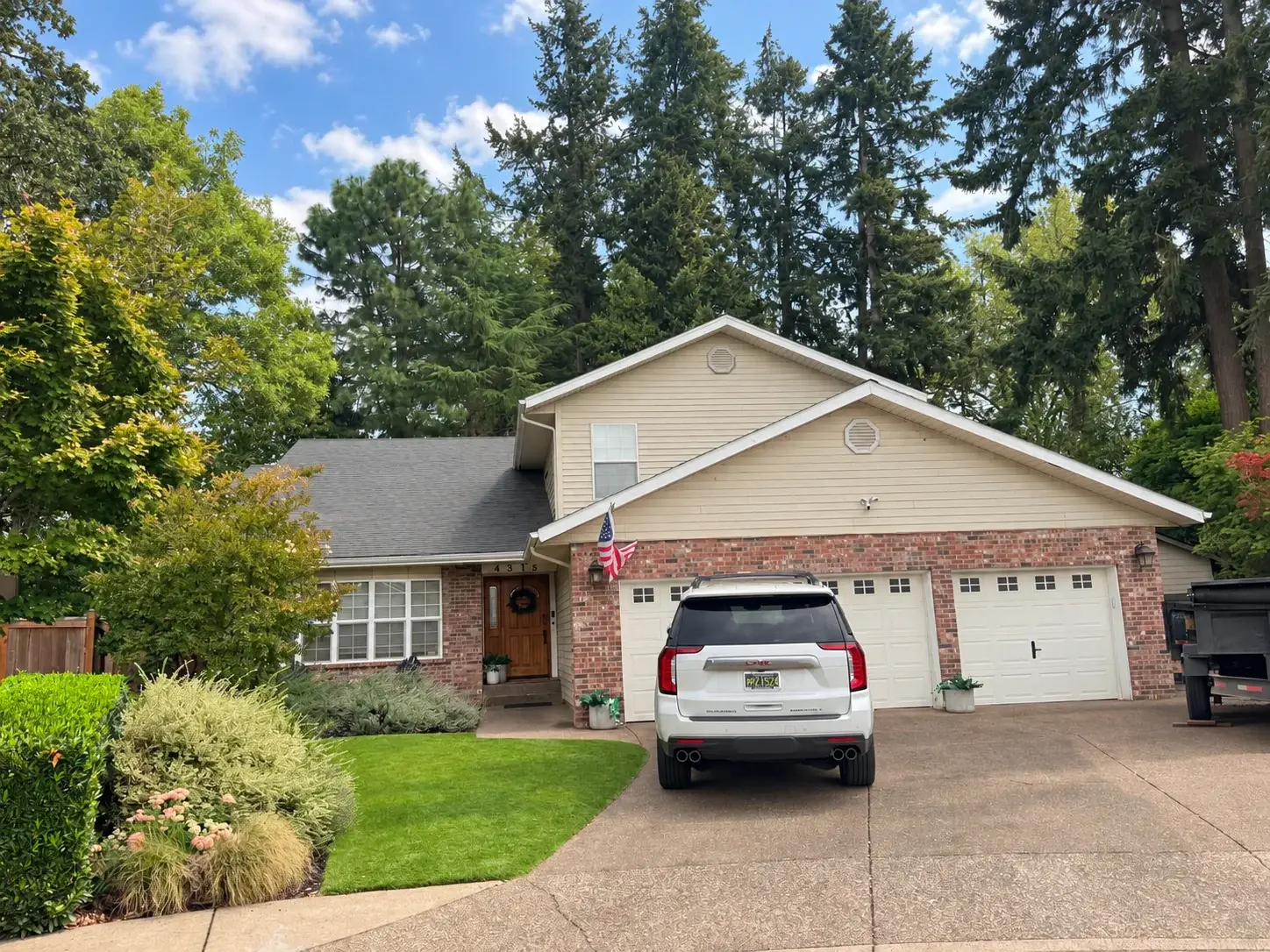 Two-story home with a three-car brick garage under tall fir trees